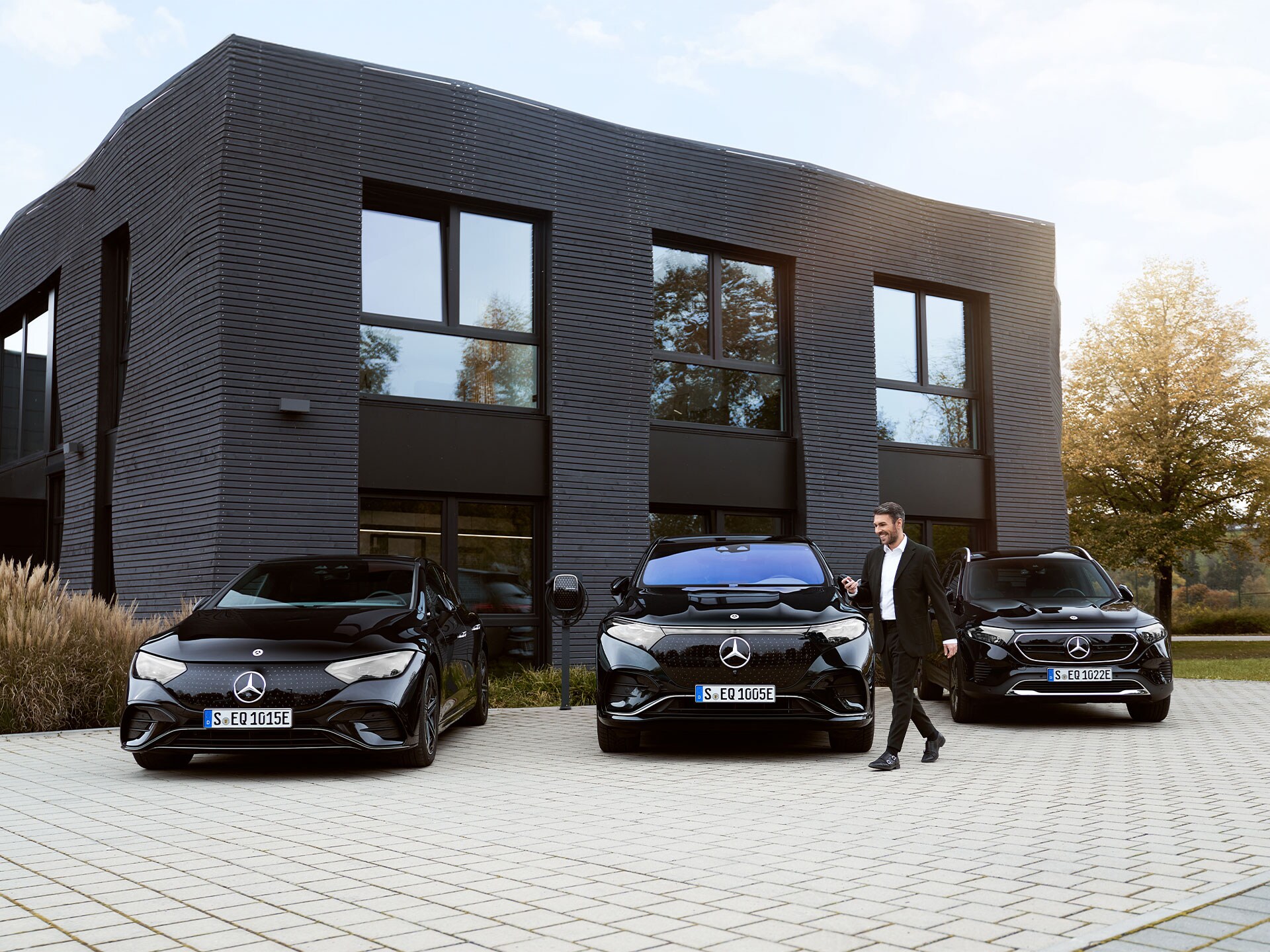 Laden am Arbeitsplatz | Laden | Mercedes-Benz Drei Mercedes-Benz Elektroautos vor einem Bürogebäude.